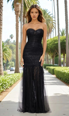A woman in the Betsy and Adam A26972 long formal dress with a strapless sweetheart neckline and black sequins stands on a palm tree-lined sidewalk in daylight.