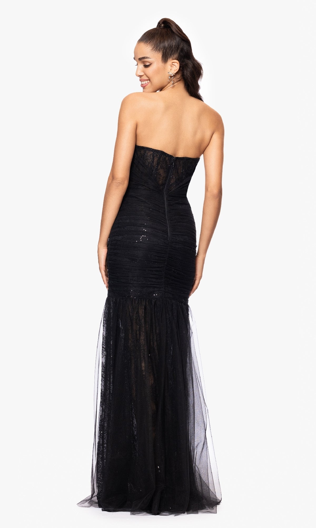 A woman, seen from the back against a white background, models the Betsy and Adam A26972 long formal dress featuring a strapless sweetheart neckline, fitted bodice, and illusion skirt in black.