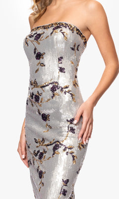 A woman poses in the Betsy and Adam A26994 long formal dress, a strapless sequin gown with purple and gold floral embroidery that sparkles elegantly against a plain white background.