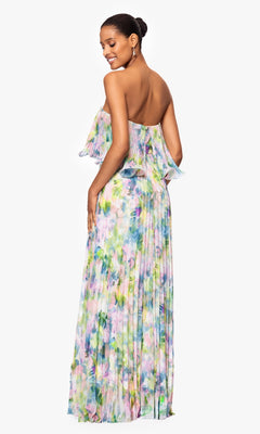 Woman wearing the Strapless Wedding Guest Gown by Betsy & Adam (style A27018), a long floral-print dress, poses with a smile and her back slightly turned—ideal attire for any wedding guest.