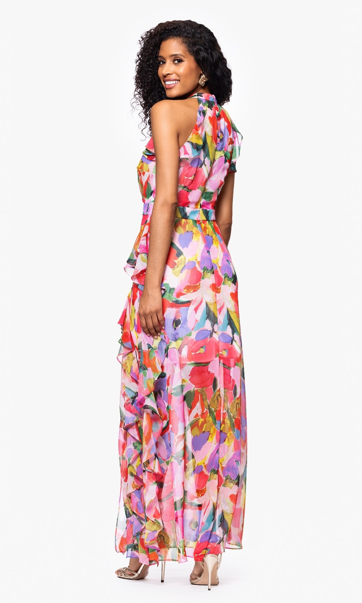Woman in the Betsy & Adam A27022 Floral Wedding Guest Dress, a sleeveless, floor-length gown with ruffle details and watercolor print, smiling and looking over her shoulder. Ideal for formal events or weddings.