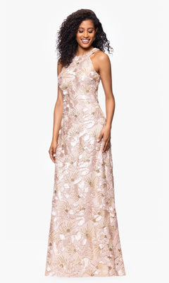 A woman poses against a plain white background, smiling in the Betsy and Adam A27023 long formal dress—a sleeveless, floor-length gown in pale pink with a floral metallic pattern and subtle sequin detailing.