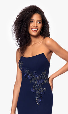 A woman models the Betsy and Adam A27030 long formal dress—navy blue, strapless, with floral embroidery and a beaded bodice—against a plain white background.