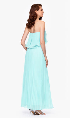 A woman in profile wears the Betsy & Adam A27098 Strapless Wedding Guest Dress—floor-length, light blue, and pleated—with silver heels, standing against a white background.
