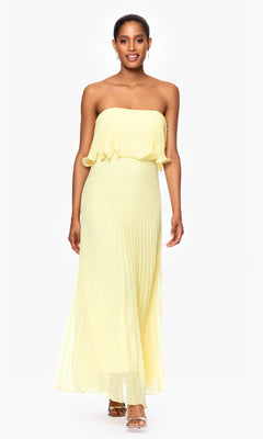 A woman models the Strapless Wedding Guest Dress: Betsy & Adam A27098 in yellow with pleats and open-toed heels, standing against a plain white background.