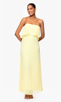 A woman stands against a plain white background wearing the Betsy & Adam A27098 Strapless Wedding Guest Dress in floor-length yellow with brown sandals.
