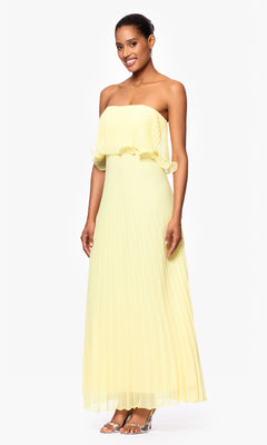 A woman stands against a plain white background wearing the Betsy & Adam A27098 strapless, floor-length, pleated light yellow wedding guest dress with clear high-heeled sandals.