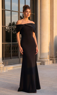 A woman wearing a black Betsy & Adam A27294 long formal dress stands outside a building with tall columns and large windows at sunset.