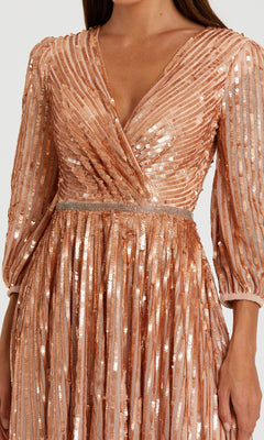 A woman wears the Mac Duggal 5509 Long Sleeve Long Formal Dress in peach, featuring a fitted waist, V-neck, and vertical and diagonal sequin patterns.