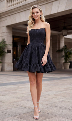 A woman in a black Nox Anabel A7019 Strapless Floral Mini Hoco Dress with a corset-style bodice and heels stands outdoors on a paved area near columned architecture.