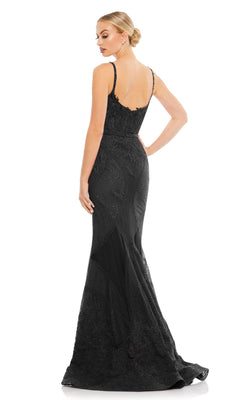 A woman in the Mac Duggal A79082 long prom dress—a fitted black gown with a beaded waistline, thin straps, and an open back—stands looking over her shoulder.