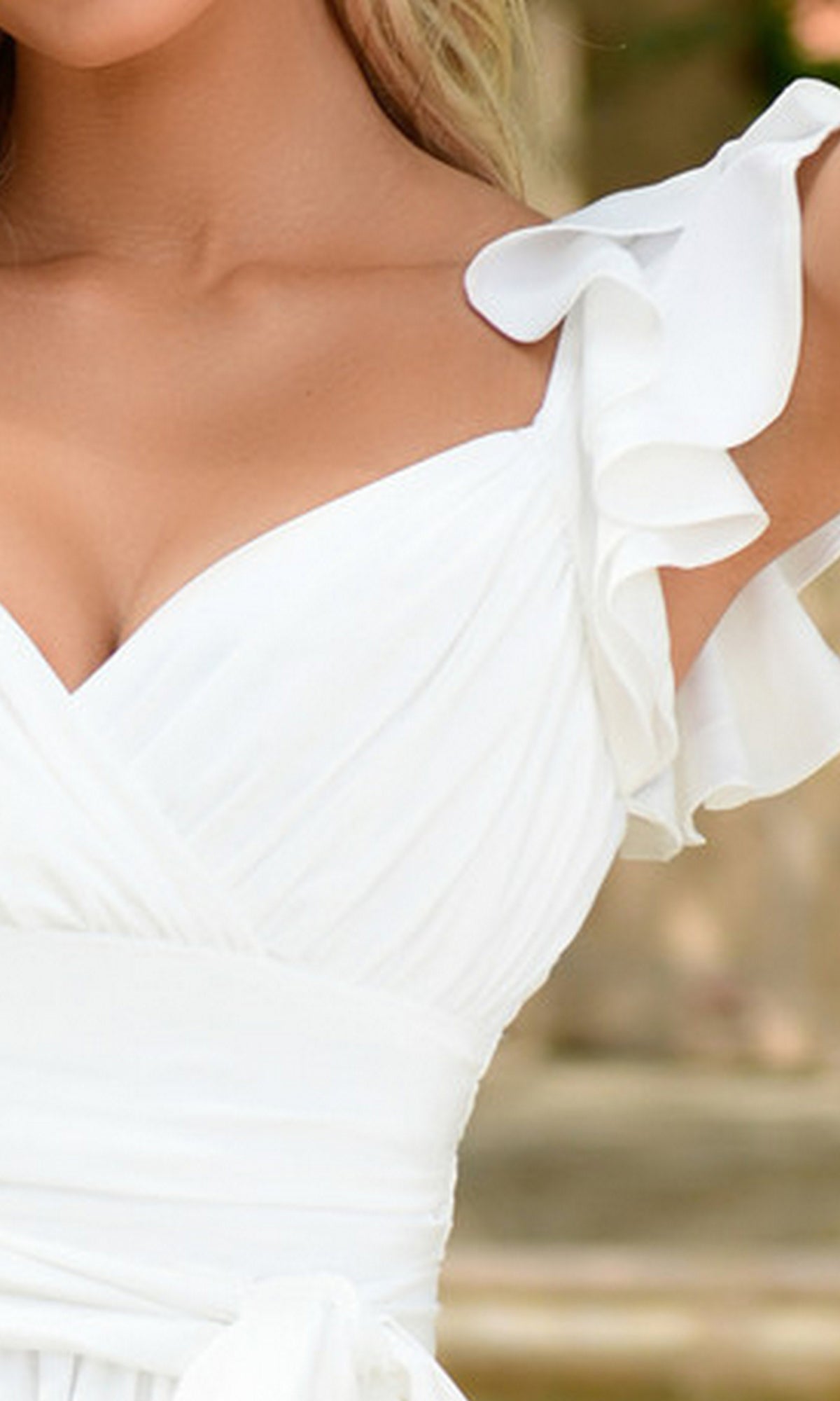 A close-up of a woman wearing the Amy Short White Graduation Dress with ruffled shoulder straps and a wrap-style bodice.