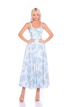 A woman stands with hands on hips, wearing the Anselma Blue Floral Cotton Summer Midi Dress and nude heels against a white background—perfect for summer weddings.