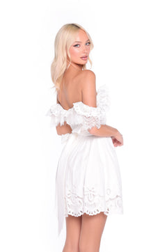 A woman with long blonde hair wears the Ari cap-sleeve short ivory graduation dress and poses against a plain white background, looking over her shoulder.