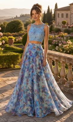 A woman stands outdoors wearing the Two-Piece Floral-Print Long Prom Dress B6803 in blue, which features a sleeveless lace crop top and a long, flowy skirt with a floral print. Elegant gardens and a grand villa create a refined backdrop that complements the sophisticated charm of this formal ensemble.