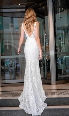 A woman with wavy hair wearing the Tina Holly BA109 white lace mermaid wedding gown stands in front of a glass revolving door.