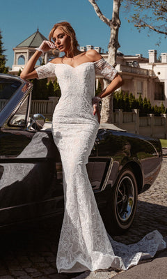A woman in the Off-Shoulder White Bridal Gown: Tina Holly BB006 leans against a black car on a cobblestone street, with a large house and trees in the background.