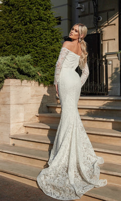 A woman stands on outdoor steps, looking over her shoulder in the stunning Long Lace White Formal Gown: Tina Holly BB007, featuring an off-the-shoulder design and long lace sleeves.