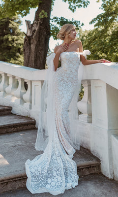 A woman in the Strapless White Wedding Gown: Tina Holly BB010 stands on outdoor stone steps by a white railing, surrounded by trees and greenery. The gown’s form-fitting lace highlights the elegance of the serene setting.