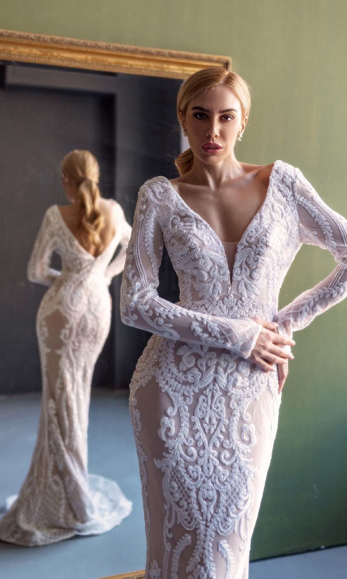 A woman stands before a mirror, showcasing both her reflection and the elegant front of the Long Sleeve White Bridal Gown: Tina Holly BB021.