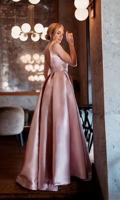 A woman in the Tina Holly BB209 Belted Long Prom Ball Gown stands indoors, glancing over her shoulder by a concrete wall and modern light fixtures.
