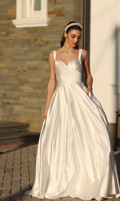 A woman wearing the Off-White Satin Prom Ball Gown: Tina Holly BB210W and a headband stands outdoors on a paved area near a stone wall.