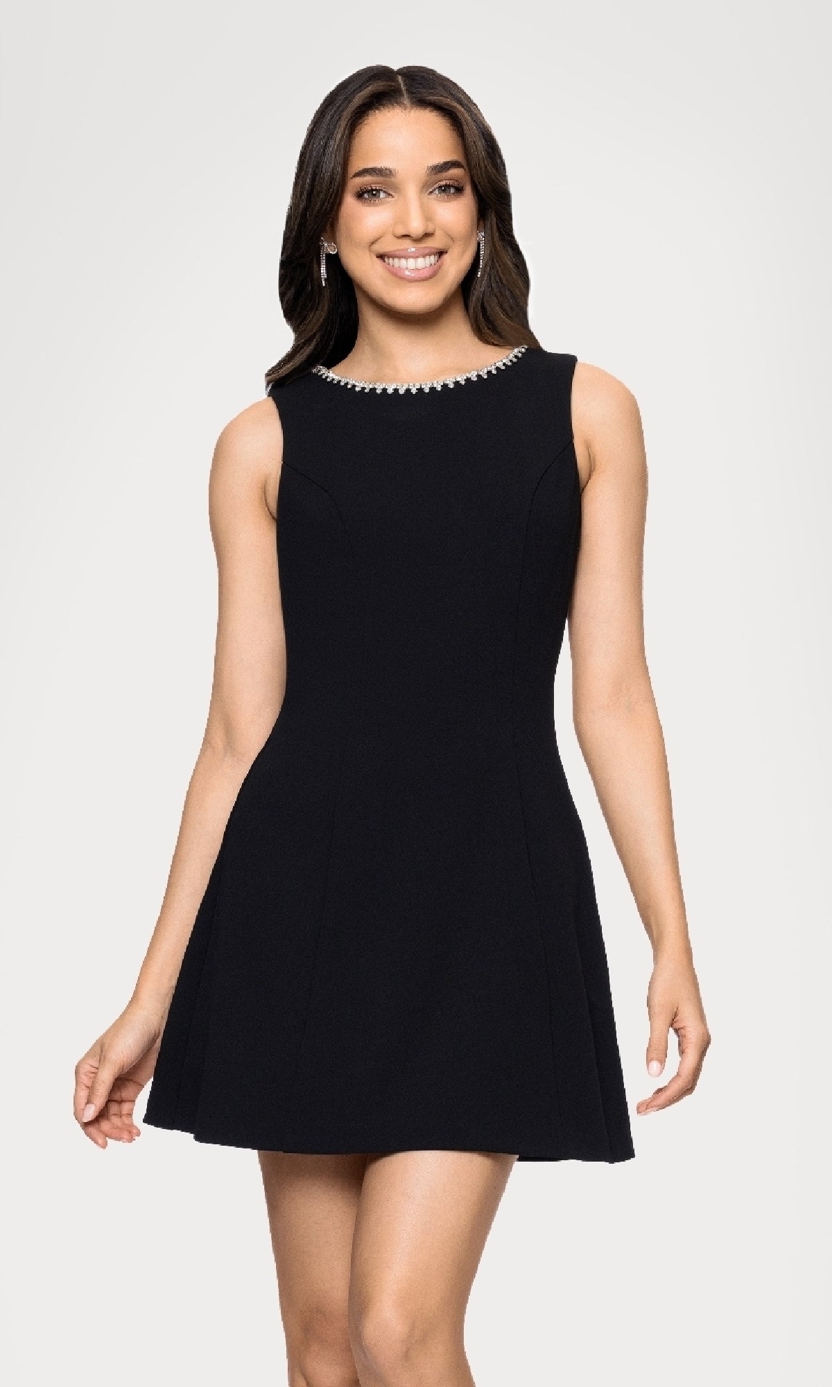 A woman stands and smiles against a white background, wearing the Blondie Nites BC164 Black Cut-Out Mini Hoco Dress—a fitted junior cocktail dress featuring a sleeveless design and jewel-embellished neckline.
