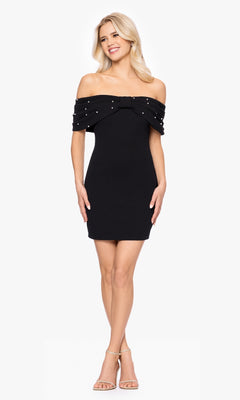 A woman models the Off-Shoulder Black Hoco Dress: Blondie Nites BC174, featuring a bow and pearl-beaded neckline, styled with strappy nude heels.