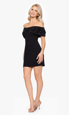 A woman smiles in the Off-Shoulder Black Hoco Dress: Blondie Nites BC174, featuring a pearl-beaded neckline, short party style, and nude high-heeled sandals that highlight its chic off-the-shoulder design.