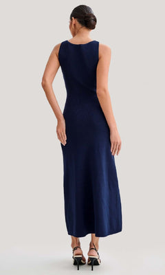 Woman stands with her back to the camera, wearing a Sleeveless Casual Button-Down Maxi Dress in navy blue and black heeled sandals against a plain light background.