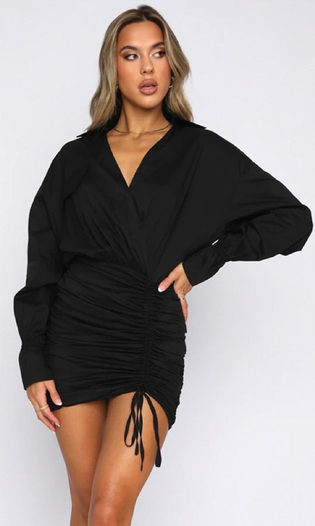 A woman stands against a plain background with one hand on her hip, wearing a black Short Casual Shirt Dress with long sleeves.