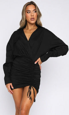A woman stands against a plain background with one hand on her hip, wearing a black Short Casual Shirt Dress with long sleeves.