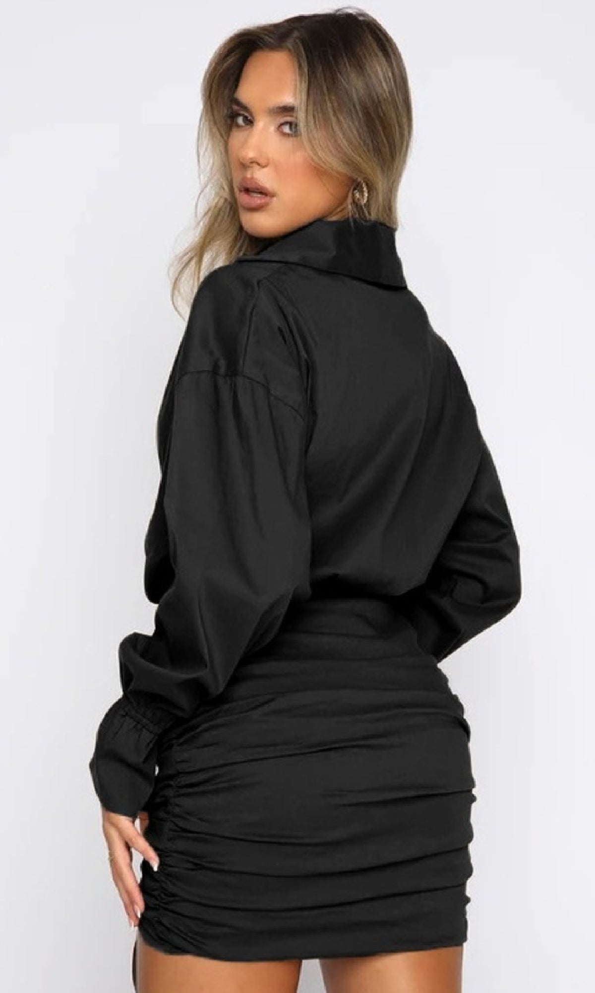 Woman in a Short Casual Shirt Dress with Long Sleeves, standing with her back to the camera and head turned over her shoulder for a chic yet casual look.