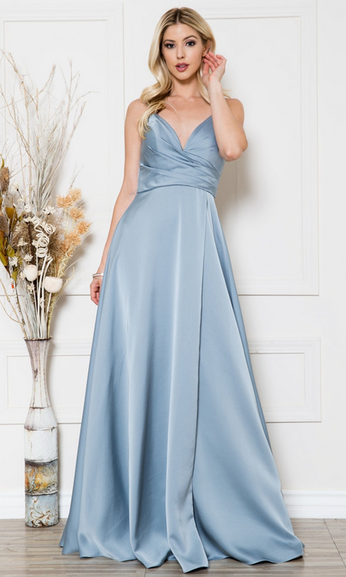 A woman in the Long Satin A-Line Formal Prom Dress BZ012 stands indoors beside a tall vase with dried flowers, set against a white paneled wall.