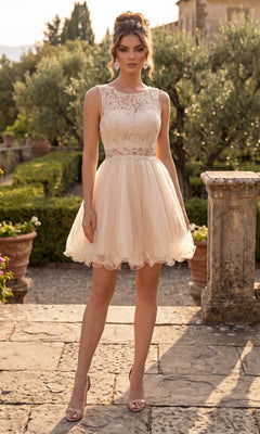 A woman stands outdoors wearing the Short Homecoming Dress: Chicas C1107 in Champagne Gold, a sleeveless knee-length dress with a lace bodice and tulle skirt, paired with nude heels. A stone walkway and lush greenery appear in the background.
