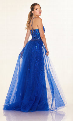 A woman models the Cecilia Couture C132 Long Prom Dress, a bright blue, floor-length sparkly gown with a tulle overskirt, standing against a plain light background and looking over her shoulder.