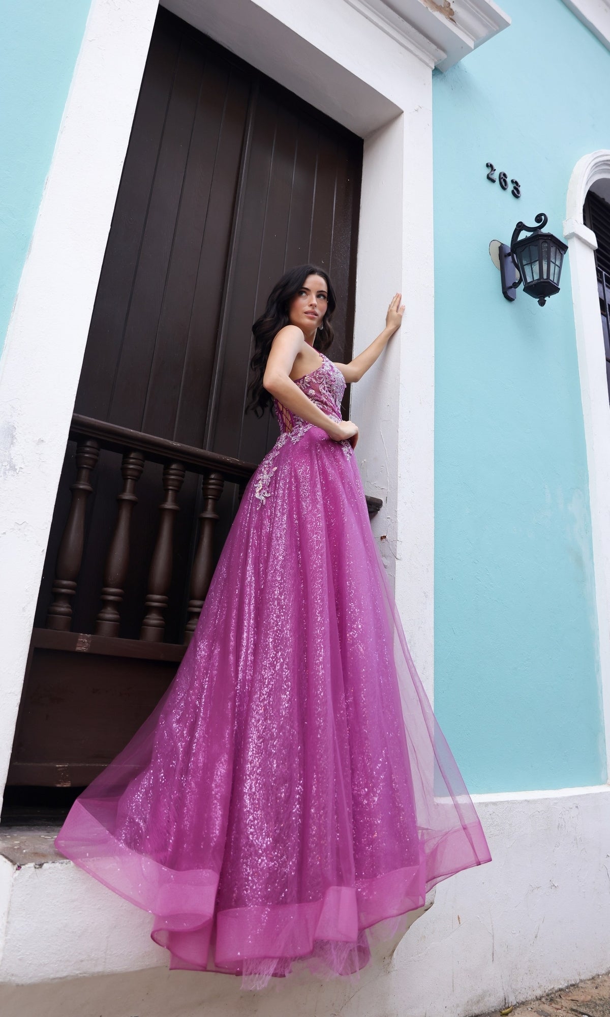 A woman in the Glitter-Tulle Long Magenta Prom Dress C1407 stands on a white ledge before a dark wooden door and turquoise wall marked with the number 263.