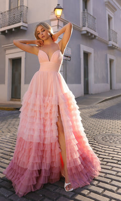 A woman in the Nox Anabel Ruffled Ombre Prom Ball Gown C1420 poses on a cobblestone street in front of a grey building with balconies.