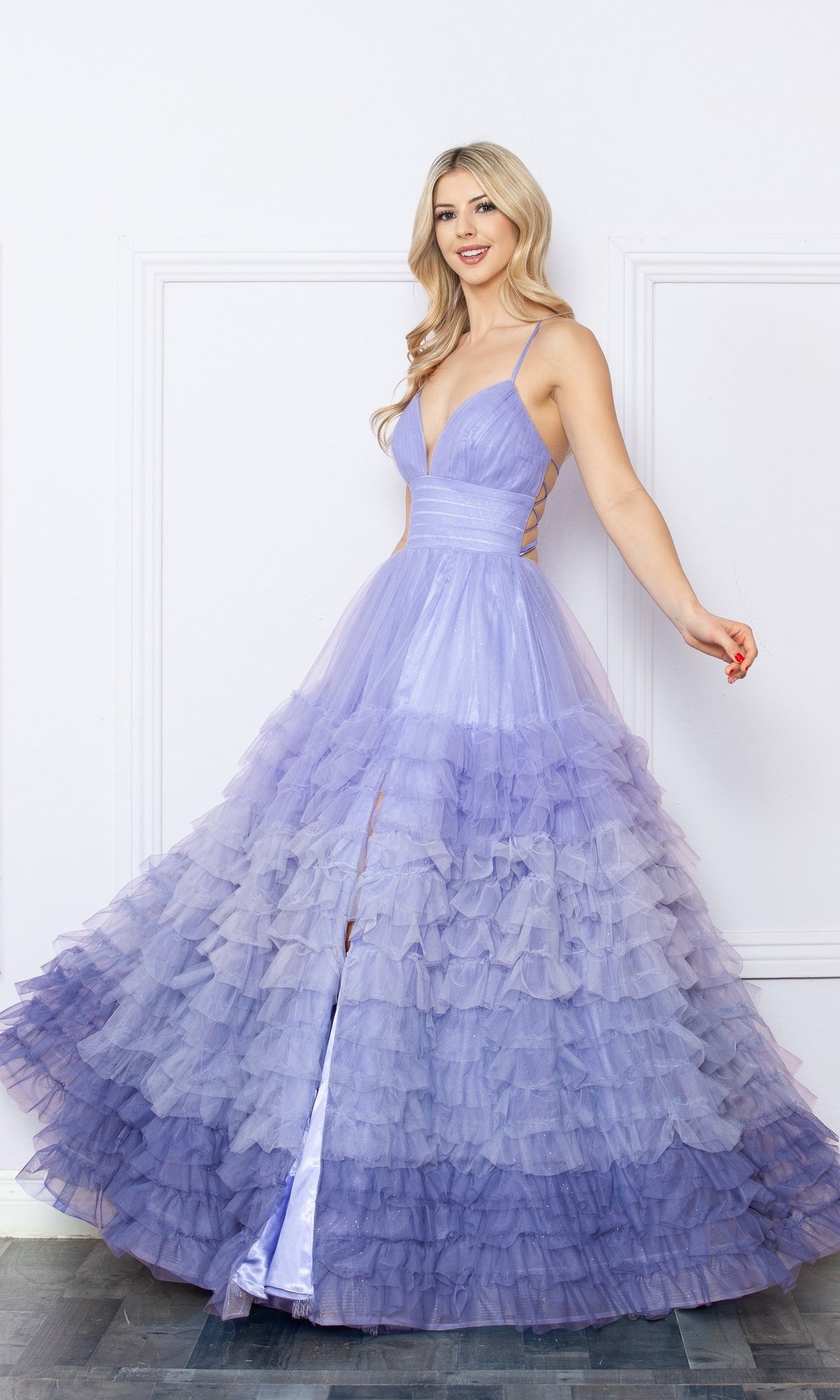 A woman poses indoors, smiling at the camera in the Nox Anabel Ruffled Ombre Prom Ball Gown C1420—a floor-length lavender dress with a deep V-neck, thin straps, and elegant ruffles.