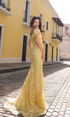 A woman wearing the Off-the-Shoulder Long Lace Prom Dress C1455 stands on a cobblestone street lined with yellow buildings and balconies, glancing over her shoulder at the camera.