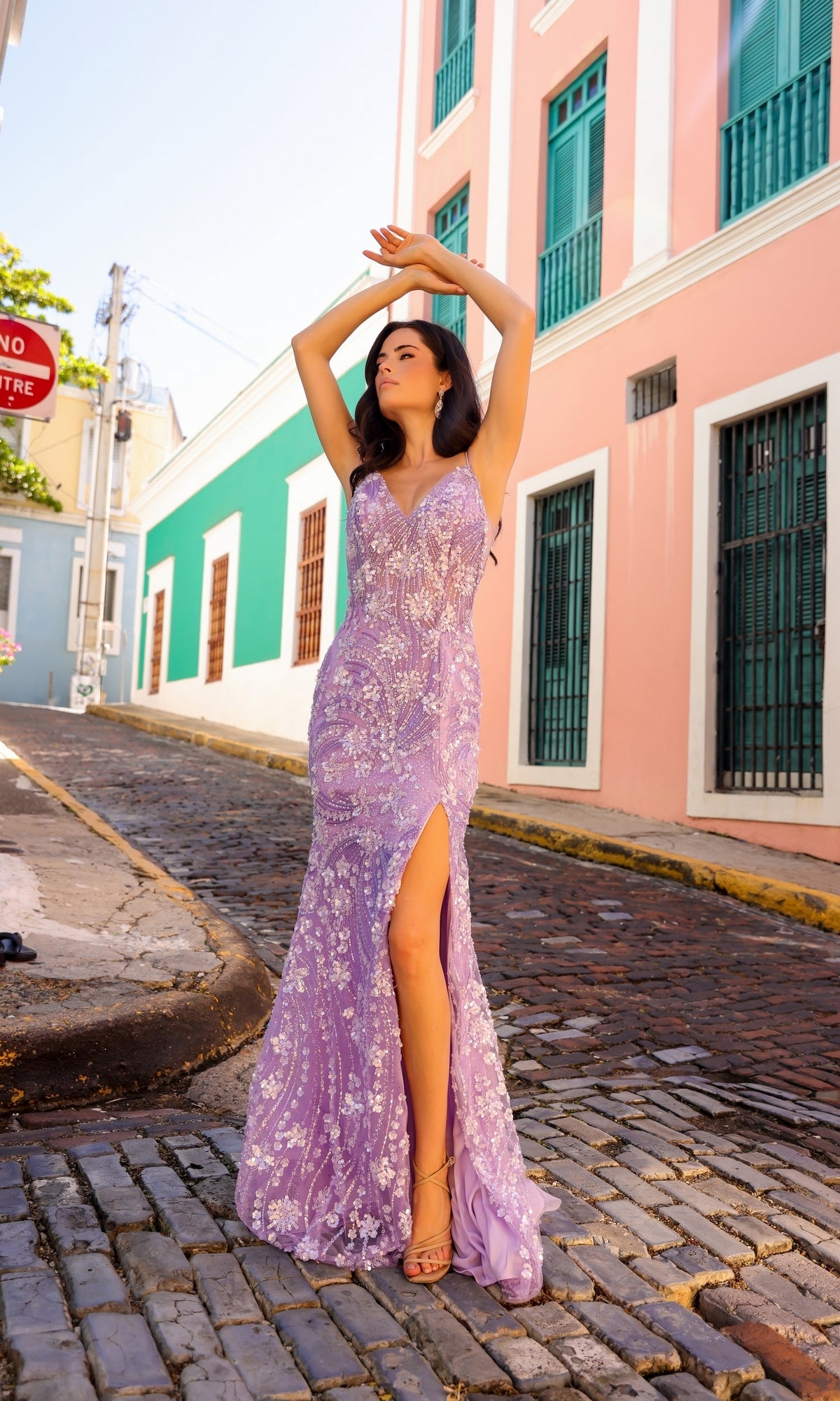A woman in the Sequin Floral-Print Long Prom Dress C1458 with a high slit stands on a cobblestone street, vibrant buildings highlighting her elegant style.