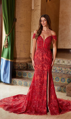 A woman poses indoors in the Nox Anabel C1600, a lace-up long beaded prom dress with an off-the-shoulder neckline, floor-length red skirt, front slit, and intricate beading, set before a tiled staircase and green curtains.