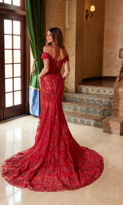 A woman stands indoors near tiled steps and green curtains, wearing the Nox Anabel C1600 Lace-Up Long Beaded Prom Dress in red, featuring an off-the-shoulder lace design and a long train, facing away from the camera.