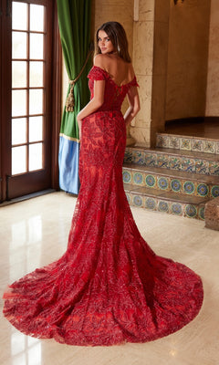 A woman stands indoors near a tiled staircase and large green-draped window, wearing the Nox Anabel C1600: a red, floor-length, off-the-shoulder lace-up long beaded prom dress with a train.