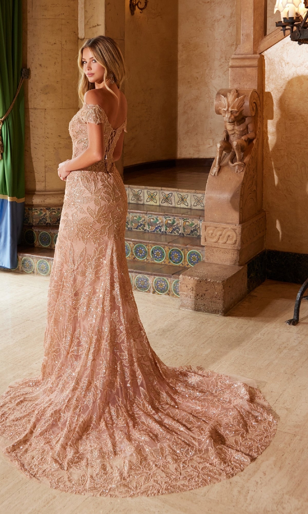 A woman stands indoors near ornate stonework and tiled steps, facing away, wearing the Nox Anabel C1600 Lace-Up Long Beaded Prom Dress with a train.