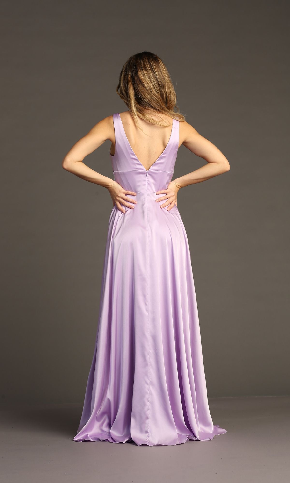 A woman in the Empire-Waist Long A-Line Prom Dress: Chicas C242, a sleeveless floor-length lavender gown, stands facing away with hands on her waist against a plain gray background.