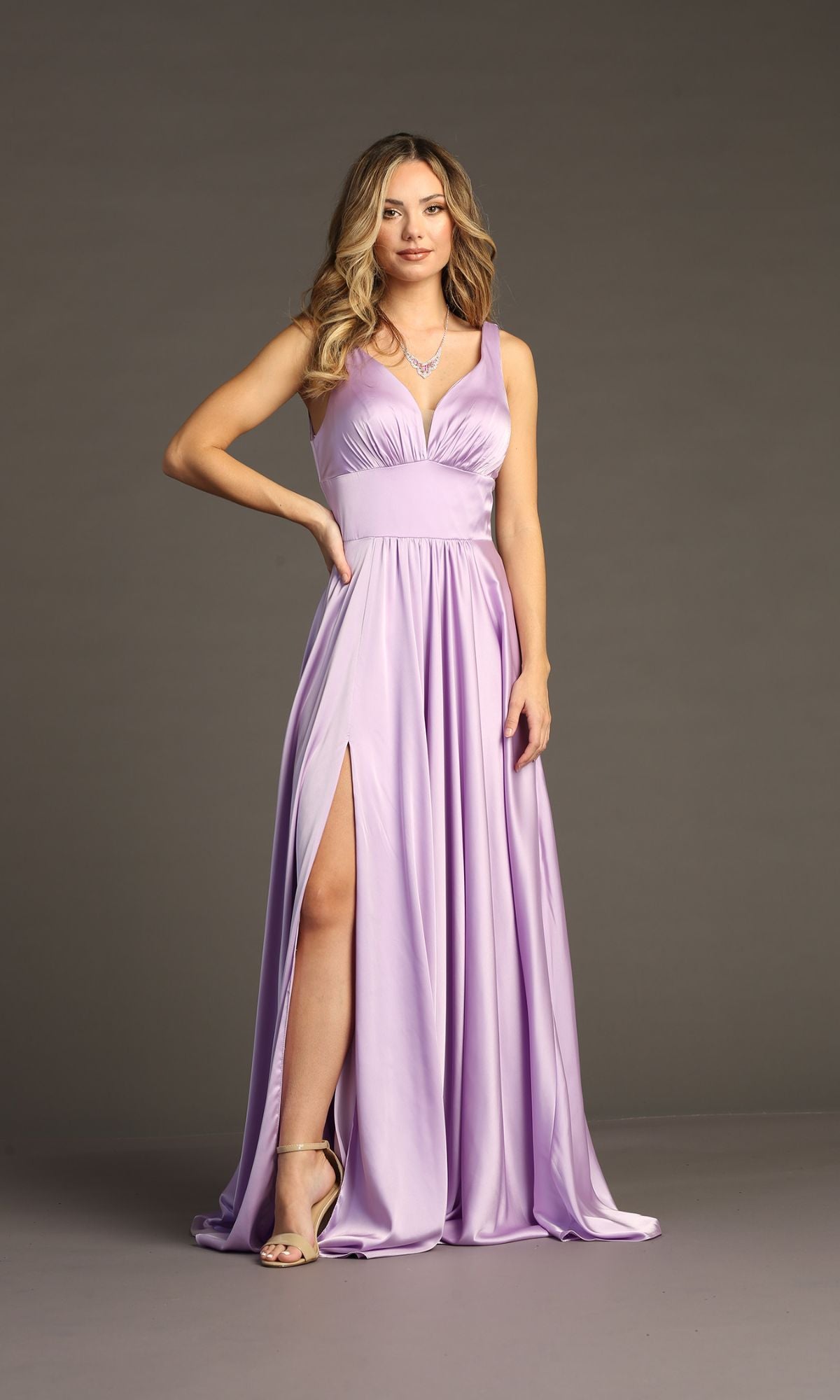 A woman stands against a plain gray background wearing the Empire-Waist Long A-Line Prom Dress: Chicas C242, a sleeveless lavender gown with a high slit that exudes elegance and sophistication for any special occasion.