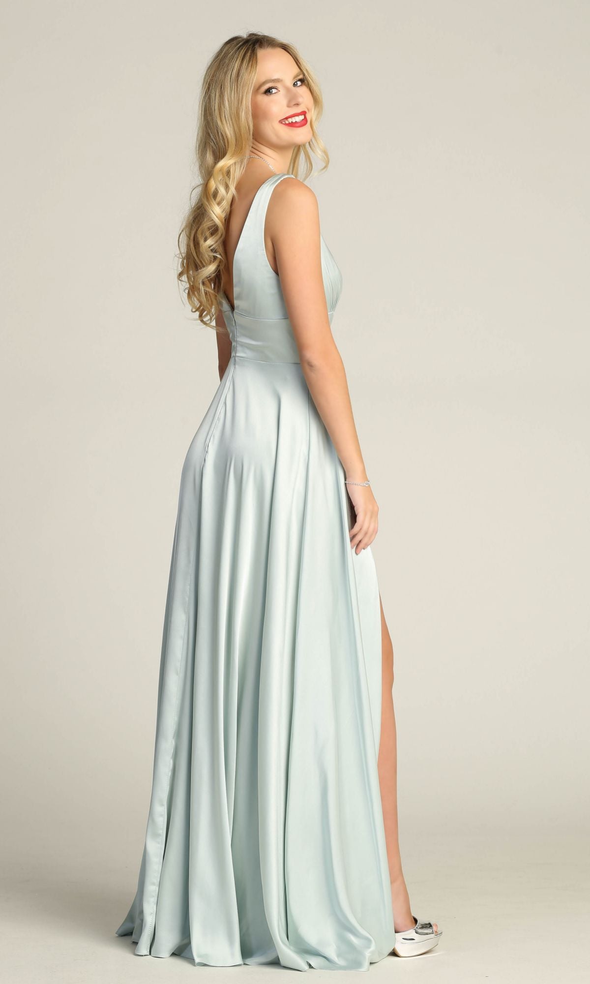 A woman with long blonde hair, wearing the Empire-Waist Long A-Line Prom Dress (Chicas C242) in light blue satin, stands sideways and smiles at the camera.