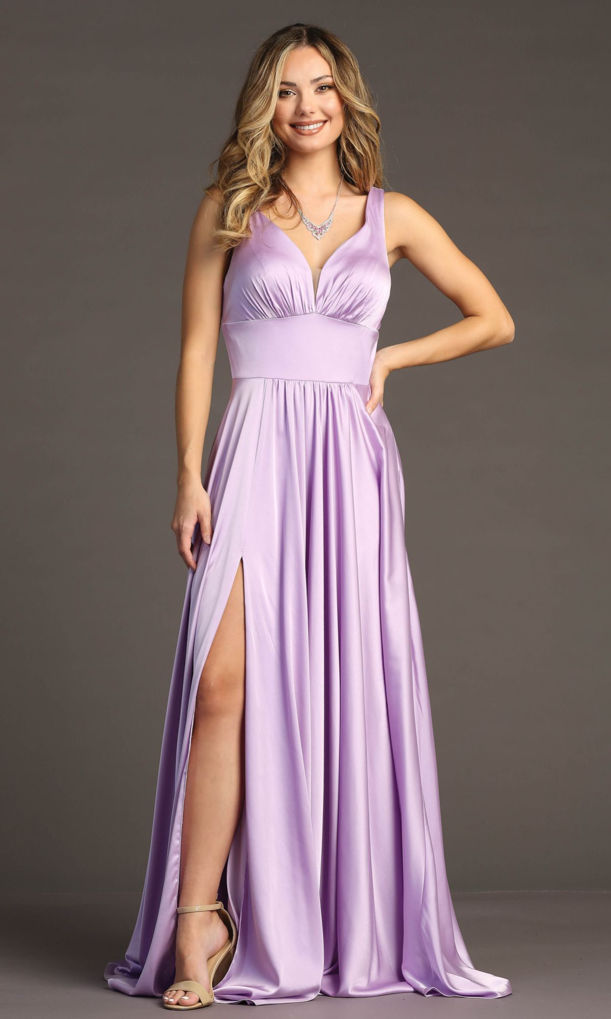 Woman wearing the Empire-Waist Long A-Line Prom Dress: Chicas C242, a sleeveless lavender gown with a V-neckline and high slit, standing and smiling against a plain background.
