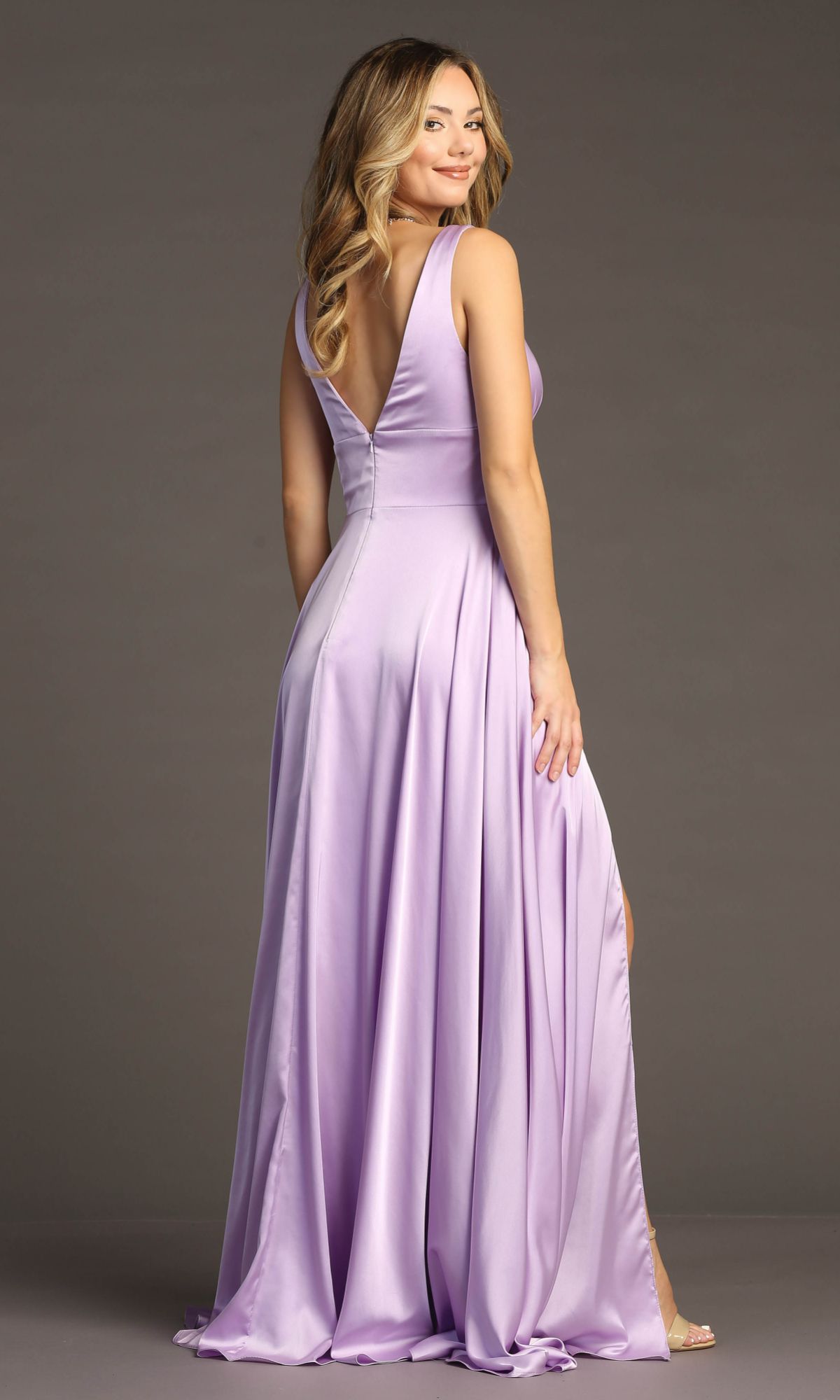 Woman wearing the Empire-Waist Long A-Line Prom Dress: Chicas C242, a sleeveless lilac gown with a deep V-back, stands and looks over her shoulder against a plain background.